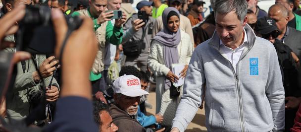 UNDP Administrator Alexander De Croo in a light gray hoodie shakes hands with a person amid a crowd outdoors.