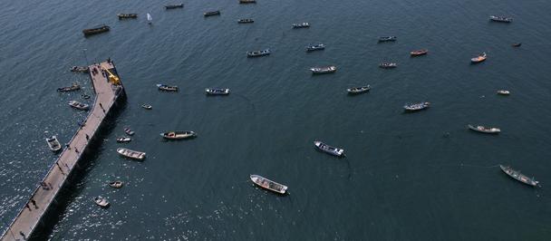 Aerial photograph of numerous boats anchored near a long jetty extending into calm blue water.
