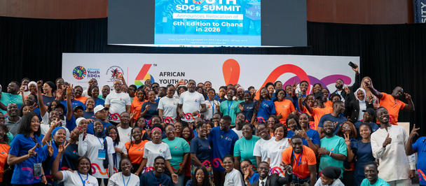Large group of people in colorful shirts posing on a stage with banners at a conference.