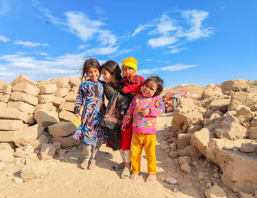 Photograph of four smiling children posing among rocky ruins under a bright blue sky.